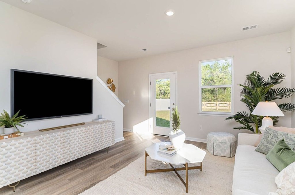 A living room with a white couch, a coffee table, and a flat screen TV mounted on the wall.