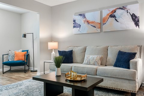 A living room with a grey couch, a blue chair, a black table, and two paintings on the wall.