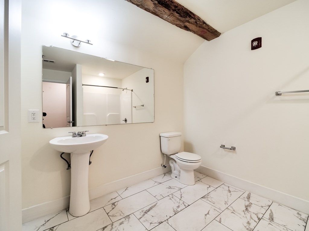 A white bathroom with a marble floor and a wooden beam on the ceiling.