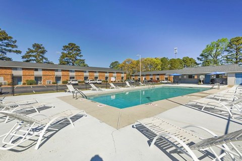 A pool surrounded by sun loungers and a building in the background.