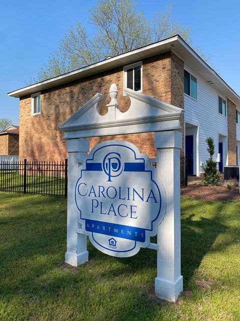A sign for Carolina Place Apartments stands in front of a brick building.