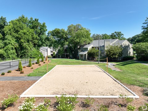 A sand volleyball court is surrounded by trees and houses.