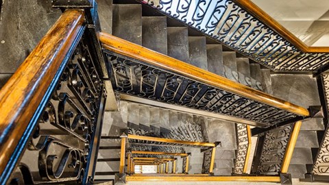 A staircase with a wooden handrail and a black metal balustrade.