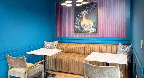 A dining area with a blue wall and a painting above a sofa.