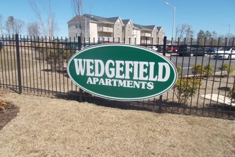 A sign for Wedgefield Apartments is shown in front of a fence and some grass.