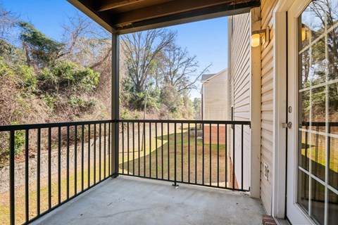 A balcony with a black railing and a view of a green lawn and trees.