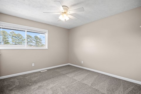 A room with a ceiling fan and a window showing trees outside.