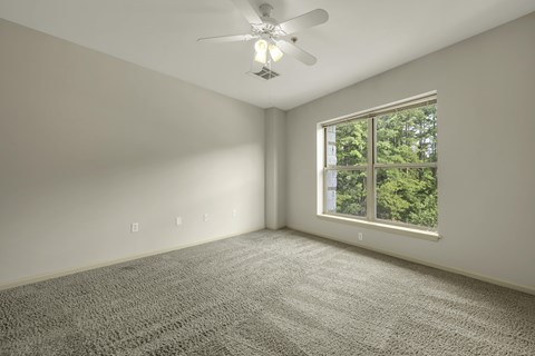 A room with a ceiling fan and a window showing trees outside.