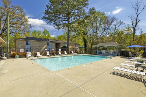 A swimming pool surrounded by trees and chairs.