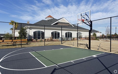 A basketball court is surrounded by a fence and a house is in the background.