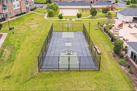 A basketball court is surrounded by a green fence and grass.