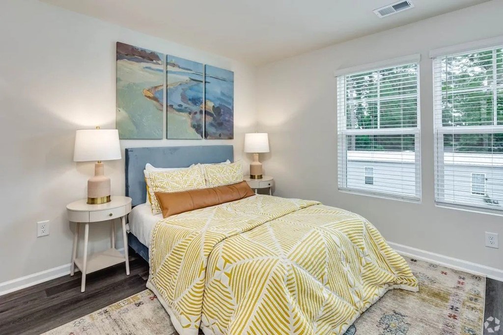 A bedroom with a bed, two lamps, and a painting on the wall.