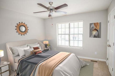 A bedroom with a bed, a mirror, a ceiling fan, and a window.