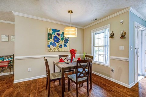 A dining room with a table set for two and a painting on the wall.