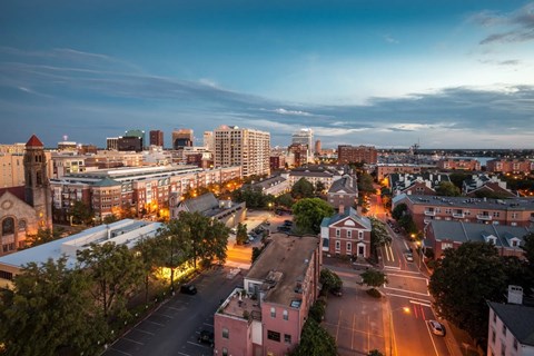 A cityscape at dusk with buildings and streets illuminated by streetlights.
