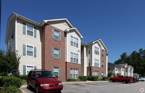 A red car is parked in front of a two-story apartment building.