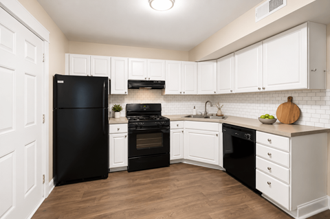 A black refrigerator stands in a kitchen with white cabinets and a white tile backsplash.