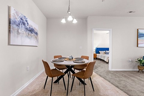 A dining room with a table set for four and a painting on the wall.
