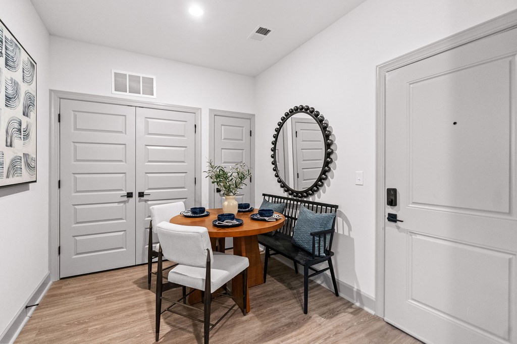 A dining room with a round mirror and a table with chairs.