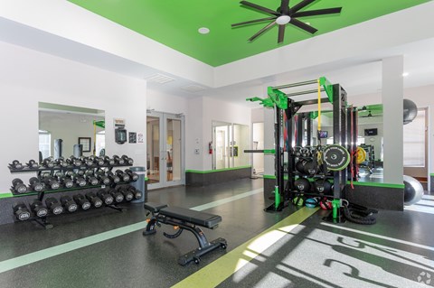 A gym with a variety of equipment including dumbbells, weight plates, and a leg press machine.