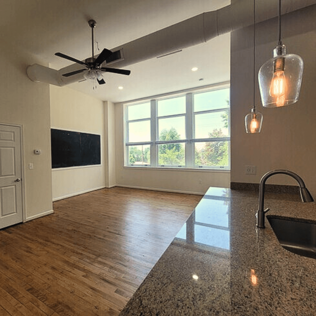 an empty living room with a large window and a kitchen