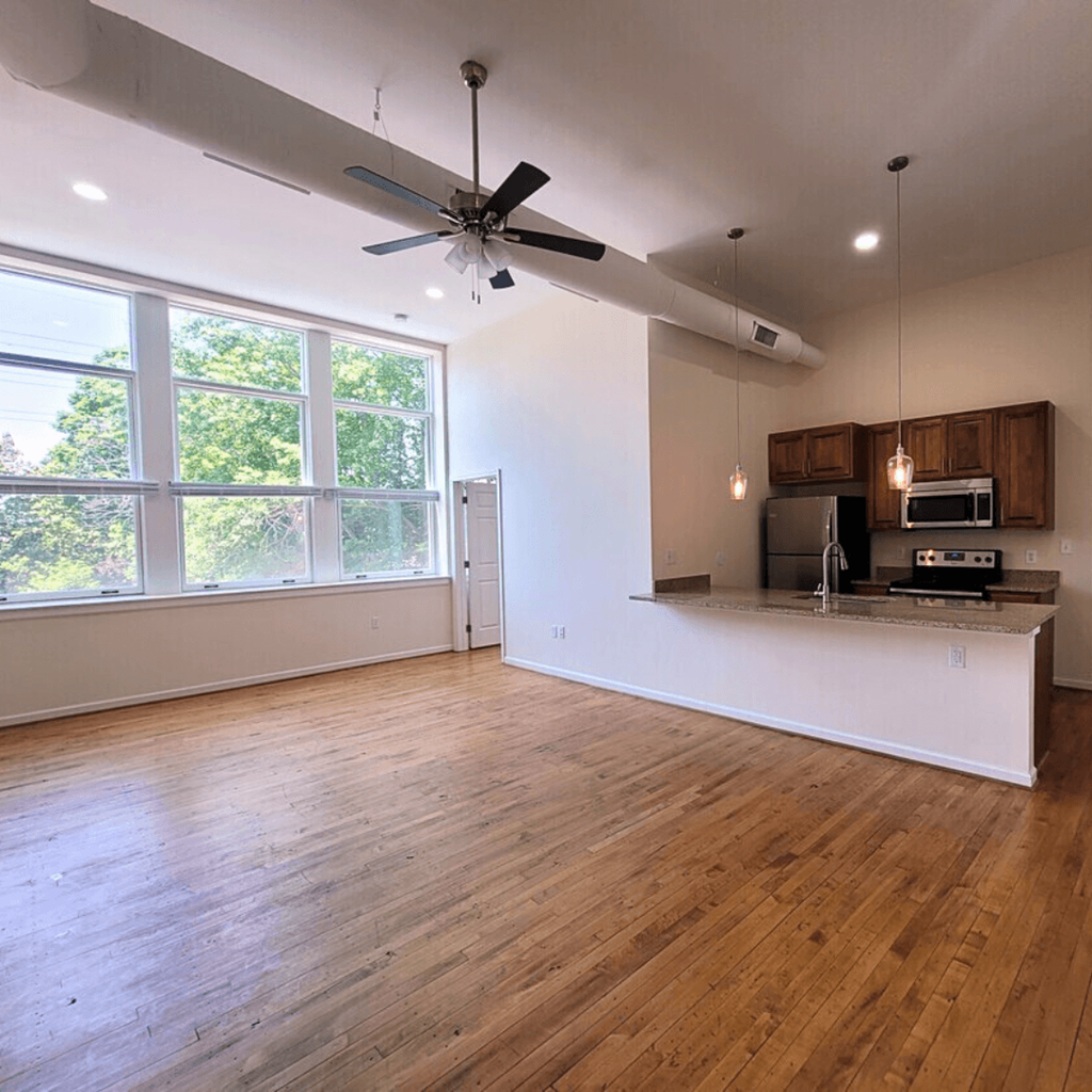 an empty living room with a kitchen and a ceiling fan