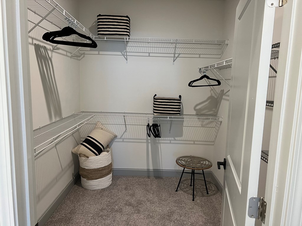 A small, white closet with a carpeted floor and a round stool.
