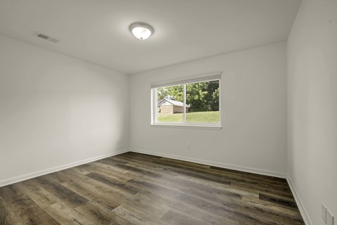 A room with wooden flooring and a window showing a house and trees outside.