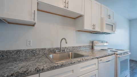 Jefferson Flats apartment kitchen with white cabinets, countertops, sink, and range.