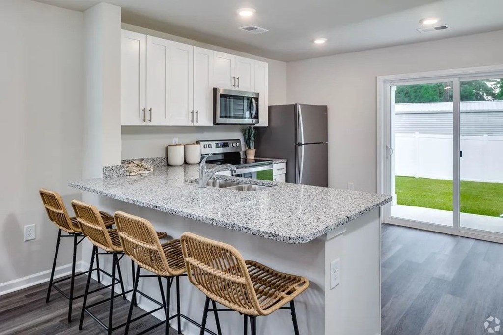 A kitchen with a granite countertop and wicker barstools.