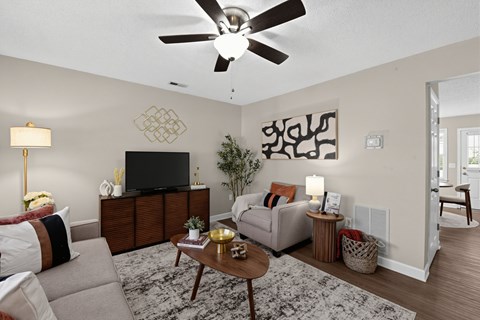 A living room with a grey couch, a coffee table, a television, and a ceiling fan.