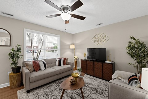 A living room with a couch, a coffee table, a television, and a ceiling fan.