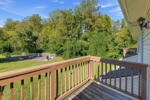 A wooden deck overlooks a grassy area with trees in the background.