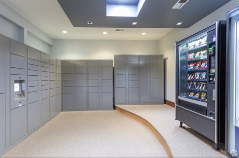 A vending machine is on the right side of a room with grey lockers.