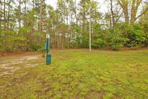 A green trash can sits in a grassy field with a sign and pole in the background.