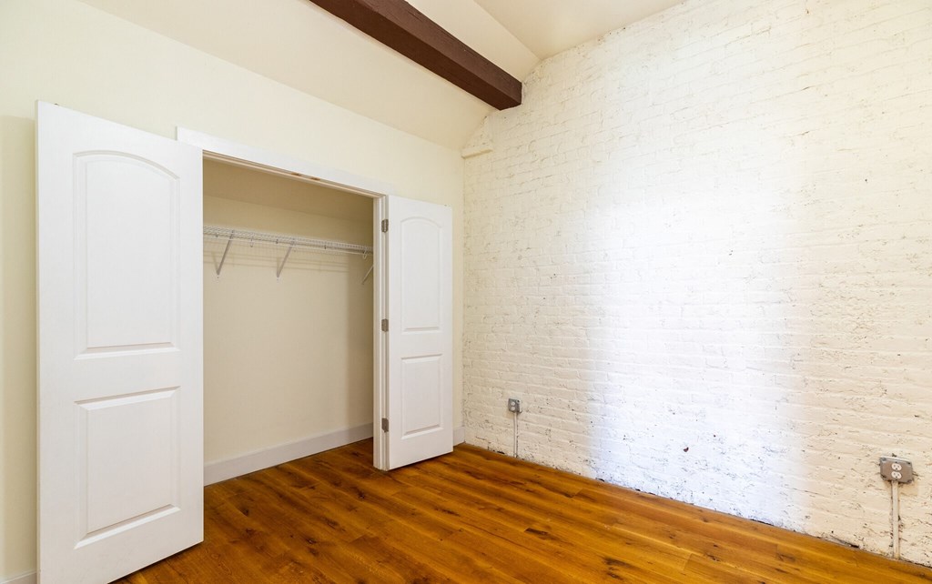 an empty room with a white brick wall and wooden floors and a closet
