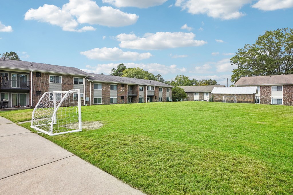 A soccer goal stands in the middle of a grassy area in front of apartment buildings.