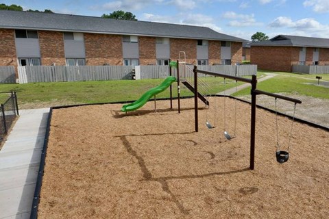 A playground with a green slide and swings in front of a brick building.