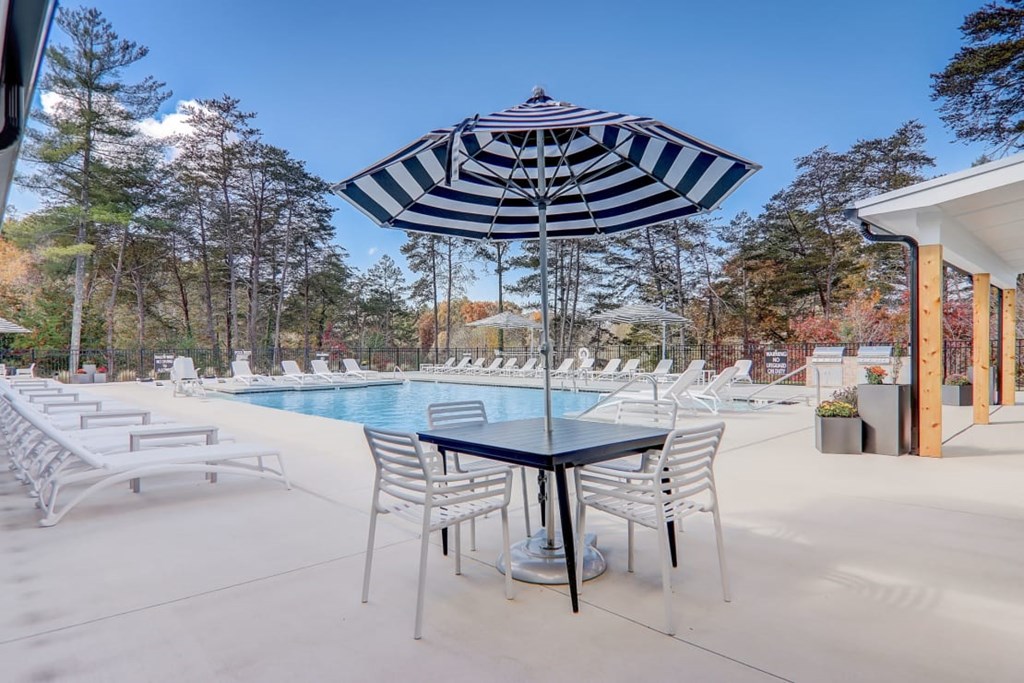 A poolside area with a table and chairs and a striped umbrella.