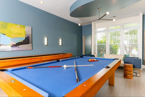 A pool table with a blue cloth and a white cue ball and red cue stick.