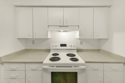 A white stove in a kitchen with white cabinets.