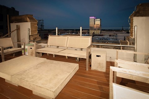 A rooftop patio with white furniture and a view of the city skyline at dusk.