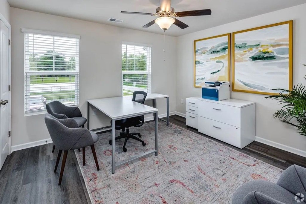 A room with a desk, chairs, and a ceiling fan.