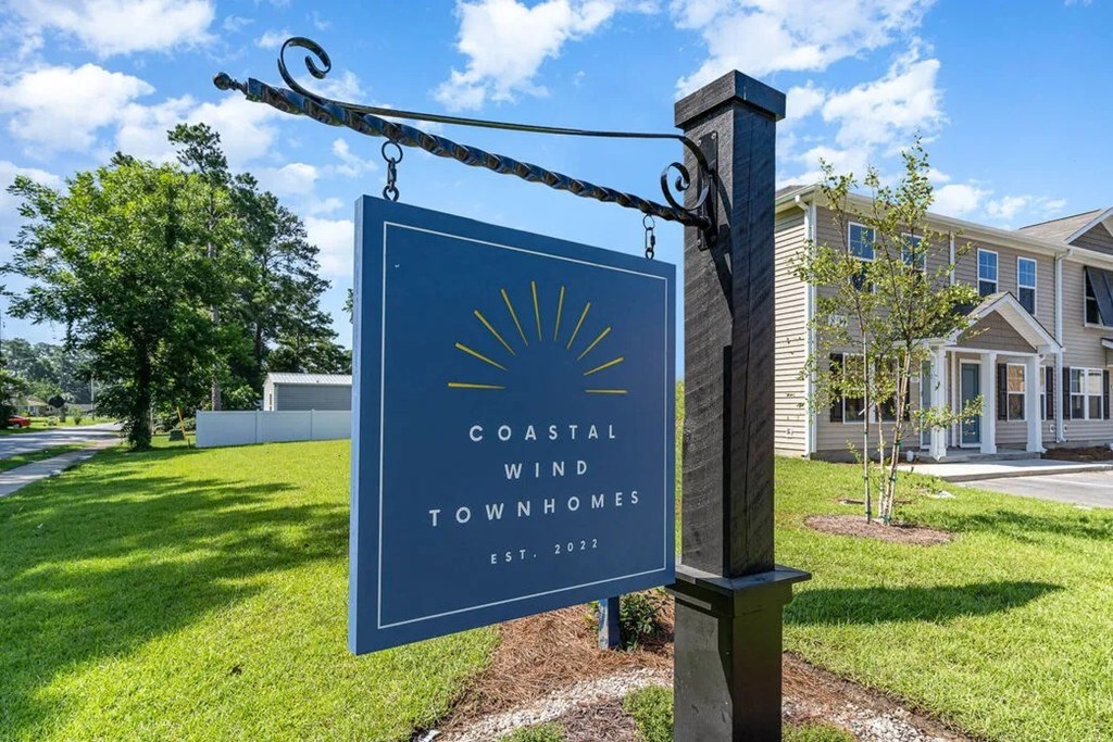 A sign for Coastal Wind Townhomes stands in front of a house.