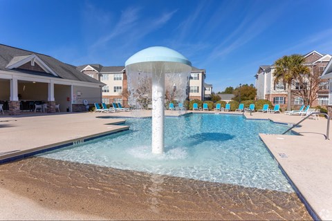 A large fountain in the middle of a pool surrounded by chairs.