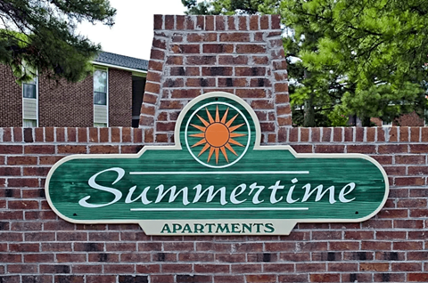 A sign for Summertime Apartments is mounted on a brick wall.