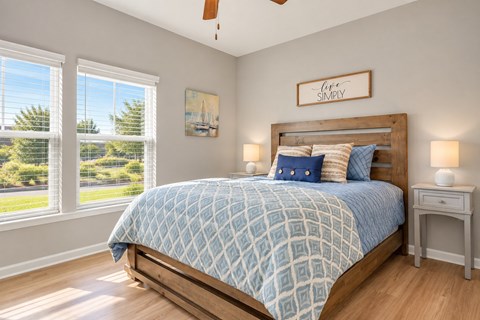 A bedroom with a bed, nightstand, and a window with a view of trees.