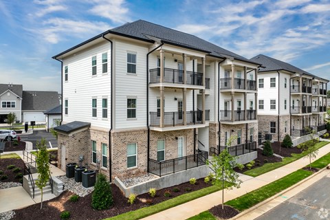 A row of modern apartment buildings with balconies and landscaped front yards.