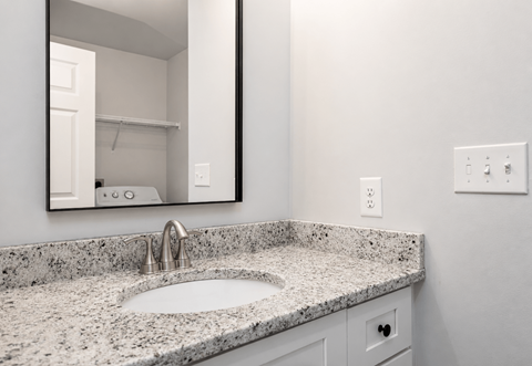 A bathroom sink with a granite countertop and a mirror above it.