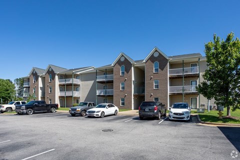 A parking lot in front of a multi-story apartment building with cars parked.